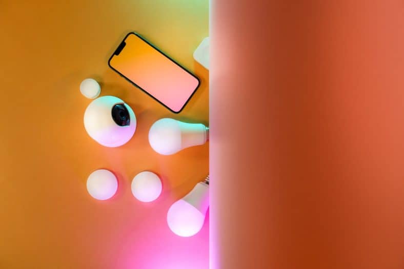 A smartphone, smart bulbs, and spherical devices are arranged on an orange surface split by a vertical sheet, creating a relaxing zen space with colorful lighting effects.